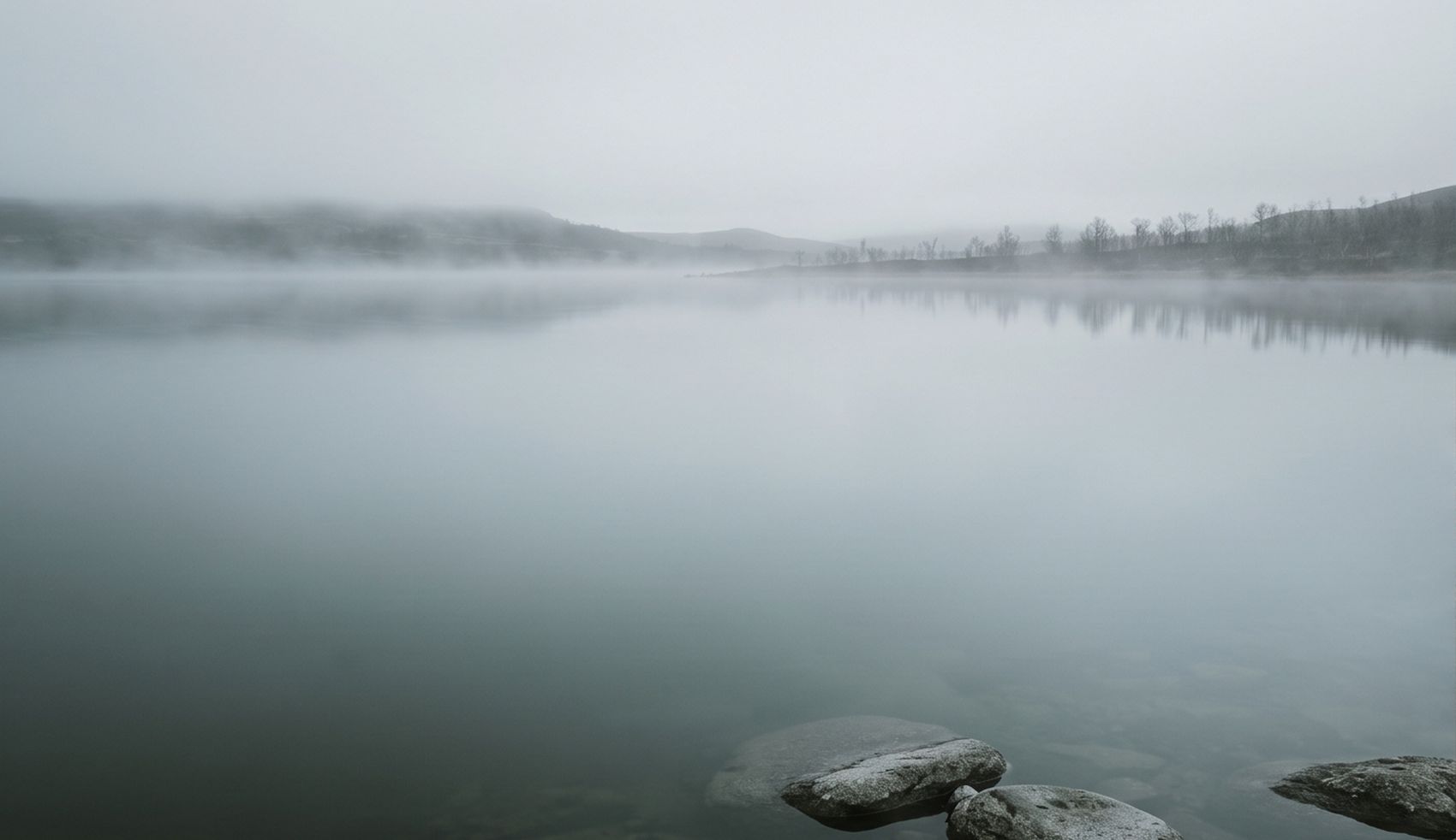 Un lac dans la brume, quelques pierres affleurant près de la rive